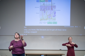 ASL interpreter signs as biology lecturer speaks at front of class
